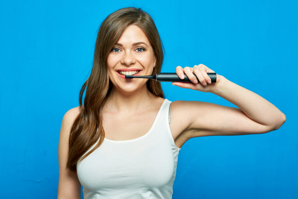 Woman brushing teeth with electric toothbrush.